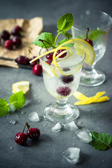 home made lemonade with cherry and lemon in a wet cold glass with ice and mint on a grey background