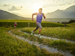 Athletes running on field path at sunset