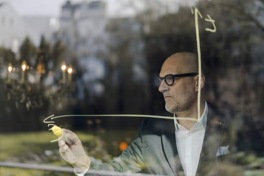 senior businessman brainstorming, drawing formulas on window pane