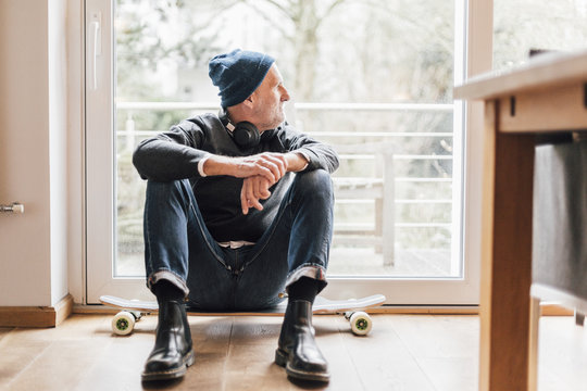 Cool senior man sitting on ground, looking out of window