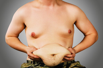 Fat body of young guy holding his belly on gray background with gradient.