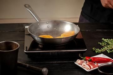 Peaches on a fry pan. Canned fruit yellow peaches, black wooden background, board.