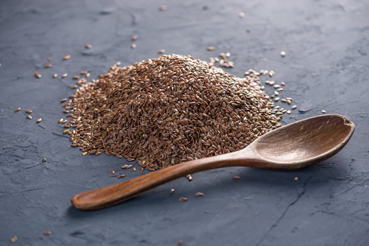 Flax seeds in a pile with spoon on a dark background. Healthy diet with omega 3 fatty acids.