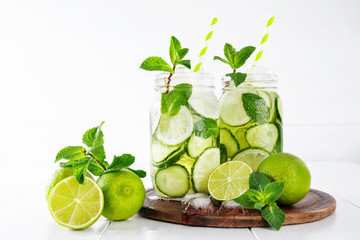 Two jars of fruit and herb infused water with cucumber, lime and mint and ice cubes on white background. The concept of detox and weight loss. Copy space