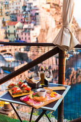 Romantic dinner for two at sunset. White wine and Tasty italian snack: fresh bruschettes  and meat on the board in outdoor cafe with amazing view in Manarola