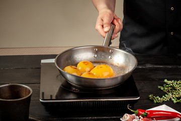 Peaches on a fry pan. Canned fruit yellow peaches, black wooden background, board.
