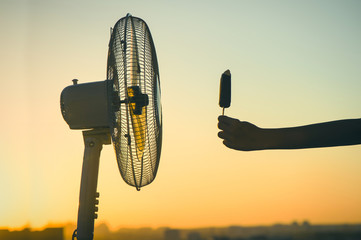 melting delicious ice cream on a stick on front of electric fan on a sunset sky background