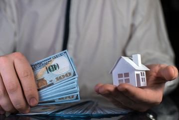 Businessman with money and paper house in his hands. Real estate selling concept