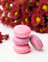Set of french macaroons on wooden table. Sweet pink and violet macaron cakes and a red chrysanthemum flowers.