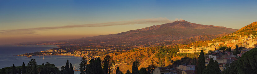 Mount Etna lit by golden sunset with trail of smoke from summit