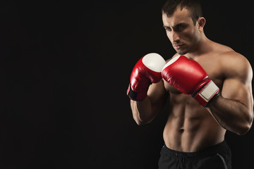 Fototapeta na wymiar Muscular man in boxing gloves at black background