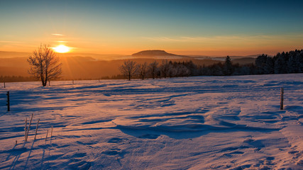 Fototapeta na wymiar Sonnenuntergang im goldenen Sonnenlicht über dem winterlichen Erzgebirge. Blick zum Scheibenberg, Fichtelberg und Keilberg.