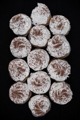 Many cupcakes on a black background. White cream and chocolate chips. View from above. Thirteen pieces.