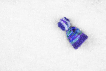 Purple wool hat/cap on the white snow with copy space. Top view.