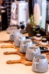 Many tea pots are assembled in a display row on wooden chopping boards in the window of a cafe