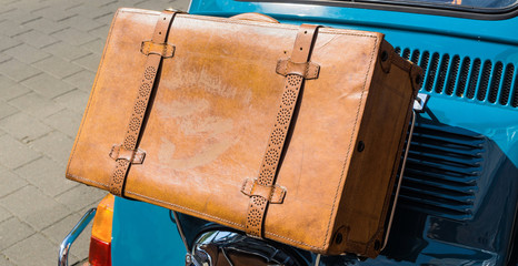 Antique brown leather case on the bridge at the bonnet flap at the back of a small car