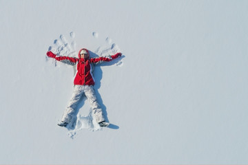 Top view of young girl is lying on the snow and making angel wings. Copy space