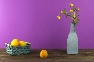 Apricots in the basket. Vase with wildflowers on a purple background. Summer mood