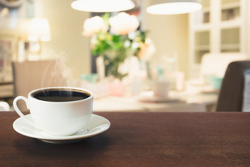 Cup of black coffee on wooden tabletop in blurred modern kitchen or cafe. Close up. Indoor.