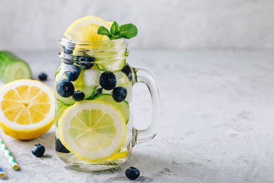 Infused detox water with lemon and cucumber slices, blueberry and mint. Ice cold summer lemonade in glass mason jar