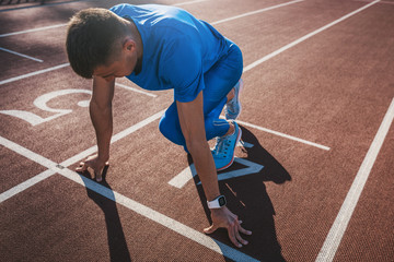 Side view of young male athlete at starting block on running track. Caucasian sprinter man in starting position for running to start a race at stadium. Sport, lifestyle and people concept.
