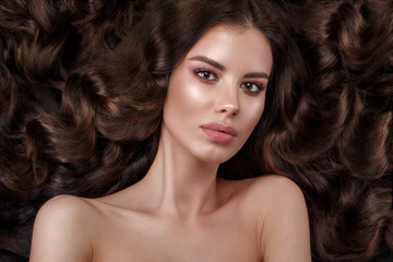 Beautiful brunette model with curls, classic makeup and full lips. The beauty of the face. Portrait shot in the studio.