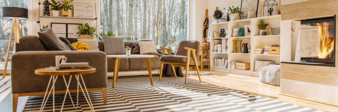 Low Angle Of A Modern Living Room Interior With A Corner Sofa, Bookshelf, Window, Striped Rug And Fireplace