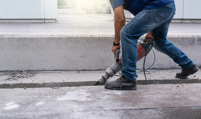 Male worker repairing driveway surface with jackhammer, digging and drilling concrete roads