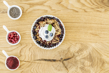 Obraz na płótnie Canvas Top view of breakfast granola with fruit, cups with pomegranate, jam and chia seeds and place for your ingredients on a wooden kitchen table