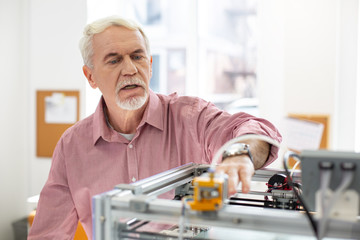 Modern technologies. Pleasant senior man running a 3D printer and printing something while working in the office