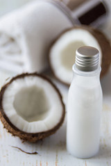 A small bottle with natural coconut oil and a fresh coconut nut on an old wooden table. Used in cosmetology for skin care of face and body.