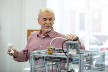 Nice job. Upbeat senior man finishing creating a model with a 3D printer and smiling contentedly...