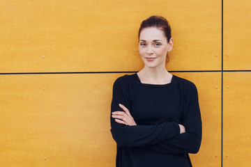 Smiling woman with folded arms against urban wall