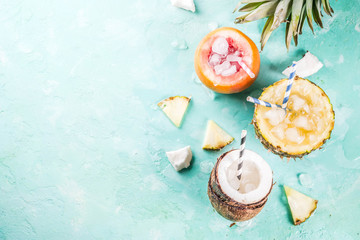 Summer holiday drink concept, set various tropical cocktails or juices in pineapple, grapefruit and coconut with ice, light blue concrete background copy space