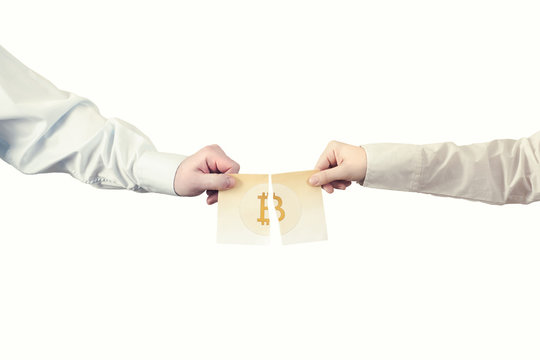 Two hands tear the paper banknote of bitcoin into two parts. Symbol BTC. Bitcoin bifurcation