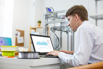 Smart ideas. Charming young man sitting at the table in the office and working on a presentation on his laptop
