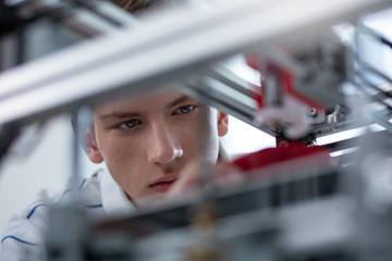 Totally immersed. Handsome young engineer being focused on 3D printing while creating another model