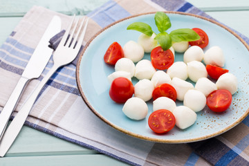 Delicious caprese salad with ripe cherry tomatoes and mini mozzarella cheese balls with fresh basil leaves.