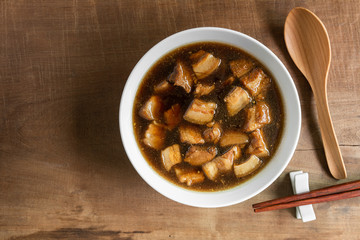 top view of boiled streaky pork with sweet brown soup in a ceramic bowl on old wooden table. asian homemade style food concept.