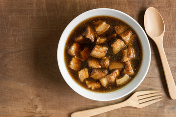 top view of boiled streaky pork with sweet brown soup in a ceramic bowl on old wooden table. asian homemade style food concept.
