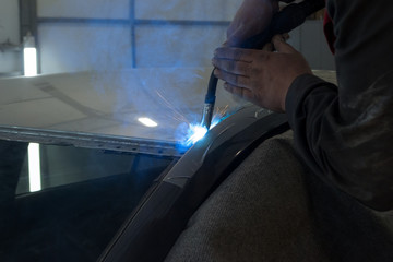Experienced man performs work on body repair car with a welding machine. Repair of the roof of the vehicle.