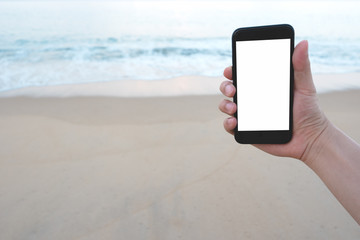 Close up man hand holding black smartphone on beautiful calm blue sea and beach background.