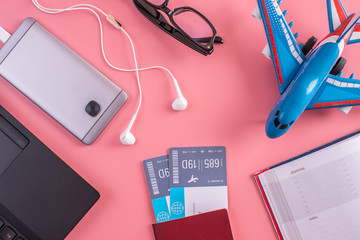 Plane, air tickets, passport, notebook and phone with headphones on pink background. The concept of preparing for travel