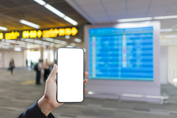 Woman hand holding smartphone mockup and blurred flight schedule background. Blank screen mobile phone for graphic display montage.
