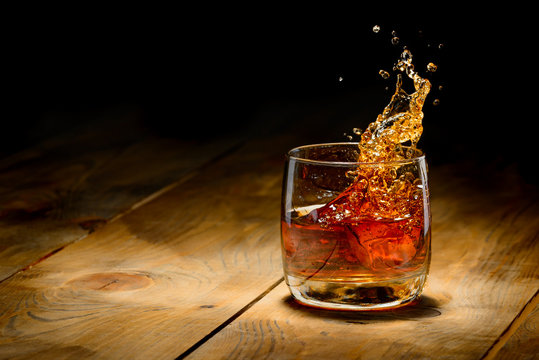 Naklejka Whiskey splash in glass on a wooden table.