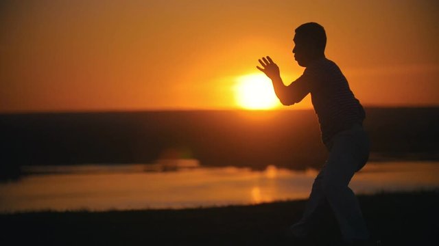 Silhouette of fighter performing capoeira tricks on the hill at summer sunset