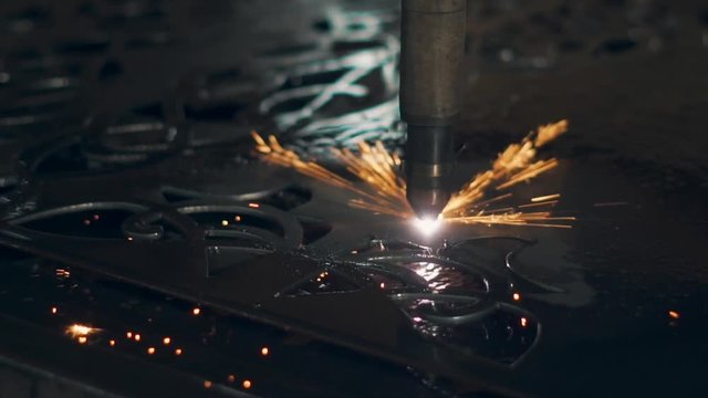 Close up shot of a programmed industrial laser machine burning through the metal. Sparks popping off the metal. Art cutting.