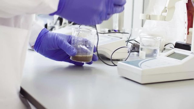Close up hands of a scientist in the laboratory measuring pH of the sample suspension by electronic pH meter