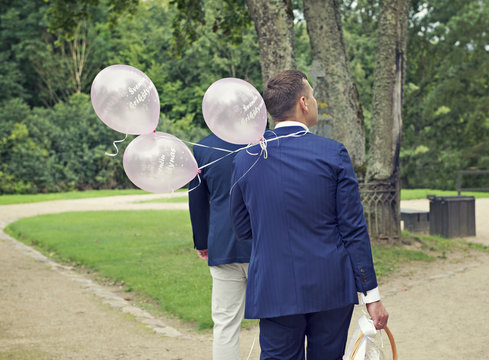 Two men standing in a park with balloons for a christening, Kernave, Lithuania