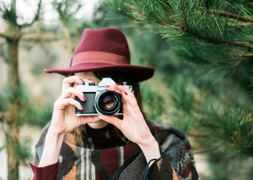 Portrait of a young Woman standing in a forest taking a photo with a vintage camera